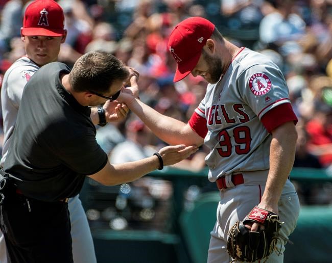 Los Angeles relief pitcher Luke Bard, right, is tended to by an unidentified trainer after being hit by a Cleveland Indians' Carlos Santana line drive during the fifth inning of a baseball game in Cleveland, Sunday, Aug. 4, 2019. (AP Photo/Phil Long)