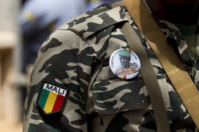 A soldier wears a button bearing the image of coup leader Capt. Amadou Haya Sanogo with the words 'President, CNRDRE,' the French acronym by which the ruling junta is known, as he stands guard at junta headquarters in Kati, outside Bamako, Mali Sunday, April 1, 2012. The leader of Mali's recent coup says he is reinstating the nation's previous constitution amid international pressure to restore constitutional order.(AP Photo/Rebecca Blackwell)
