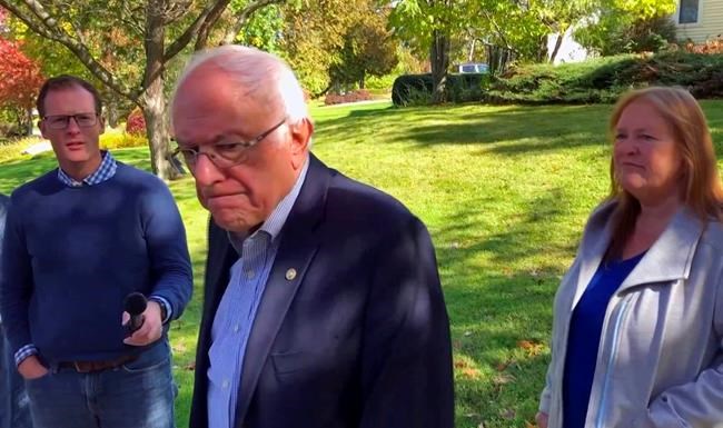 In this image taken from video, Democratic presidential candidate Sen. Bernie Sanders, I-Vt., speaks we reporters outside his home, Tuesday, Oct. 8, 2019, in Burlington, Vt. His wife, Jane O'Meara Sanders listens at right. Sanders says he was