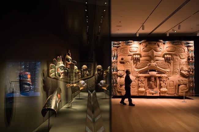 First Nations masks are displayed behind glass as a man walks past