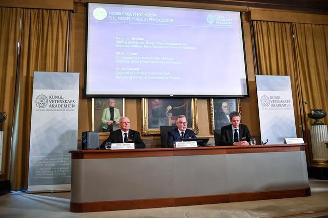 Goran K Hansson, centre, Secretary General of the Royal Swedish Academy of Sciences, and academy members Mats Larsson, left, and Ulf Danielsson, announce the winners of the 2019 Nobel Prize in Physics, during news conference at the Royal Swedish Academy of Sciences in Stockholm, Sweden, on Tuesday Oct. 8, 2019. The 2019 Nobel Prize in Physics is awarded to James Peebles, Michel Mayor and Didier Queloz. (Claudio Bresciani / TT via AP)