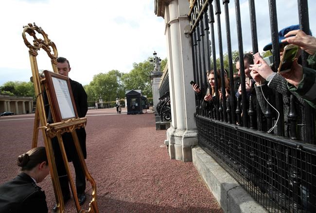People gather outside the gates of Buckingham Palace to take pictures of the official notice to formally announce the birth of a baby boy to Prince Harry and Meghan Duchess of Sussex, set on an easel in the forecourt of Buckingham Palace in London, Monday May 6, 2019. The official announcement is traditionally placed on public view in the courtyard of the palace. (Yui Mok/PA via AP)