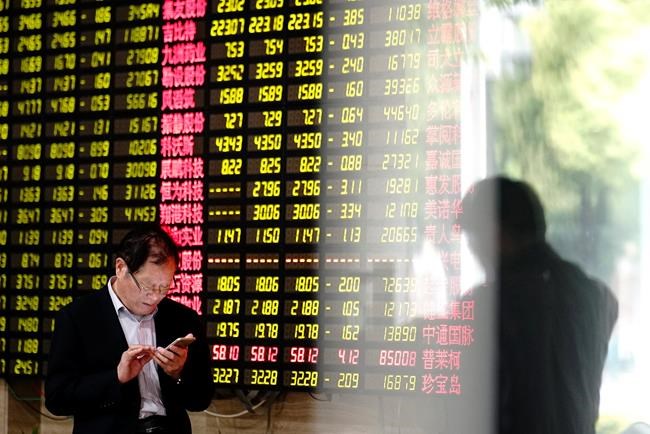 A man looks at his smartphone near a display showing stock prices at a brokerage house in Shanghai Monday, May 6, 2019. China's benchmark Shanghai Composite index dives on U.S. President Donald Trump threat of more China tariffs. At right is a reflection off a display board. (AP Photo)