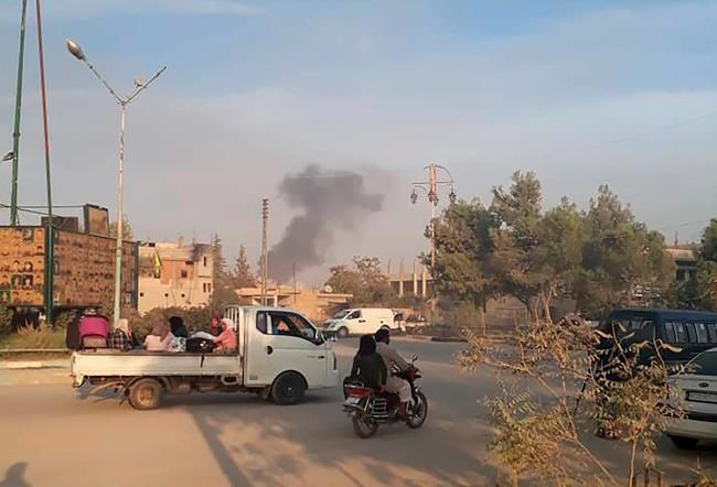 In this photo provided by Rojava Media Center, a pro-Kurdish media group, Syrians flee as smoke rises from shelling by Turkish forces, in Ras al Ayn, northeast Syria, Wednesday, Oct. 9, 2019. Turkish President Recep Tayyip Erdogan announced Wednesday the start of a Turkish military operation against Kurdish fighters in northeastern Syria. (Rojava Media Center via AP)