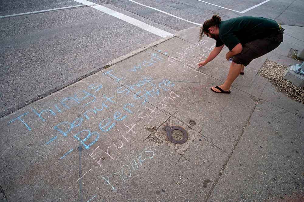 Daniel Crump / Winnipeg Free Press
Jaret Olford, a community resident and member of the Concerned Voters Group, writes a list of ideas about what the boarded and neglected Rubin Block building could be used for during a Chalk Party, at the corner of Osborne and Morley, Wednesday.