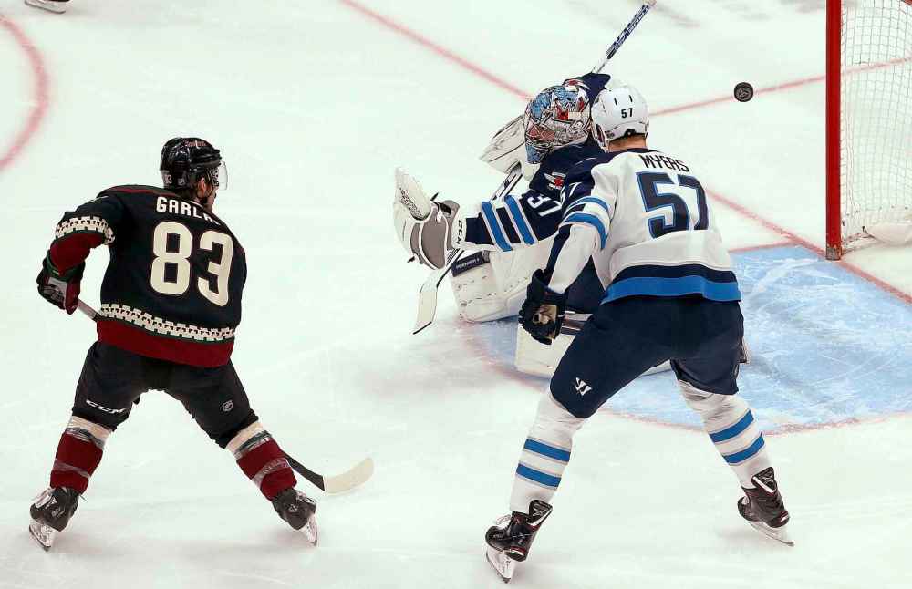 Winnipeg Jets goaltender Connor Hellebuyck (37) gives up a goal to Arizona Coyotes' Alex Galchenyuk as Jets defenseman Tyler Myers (57) and Coyotes right wing Conor Garland (83) watch during the first period of an NHL hockey game Saturday, April 6, 2019, in Glendale, Ariz. (AP Photo/Ross D. Franklin)