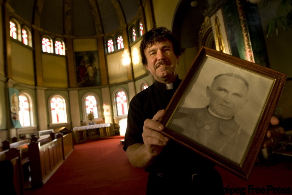 PHIL.HOSSACK@FREEPRESS.MB.CA
Father Taras Kowch with a portrait of his heroic grandfather, Father Emilian Kowcz.