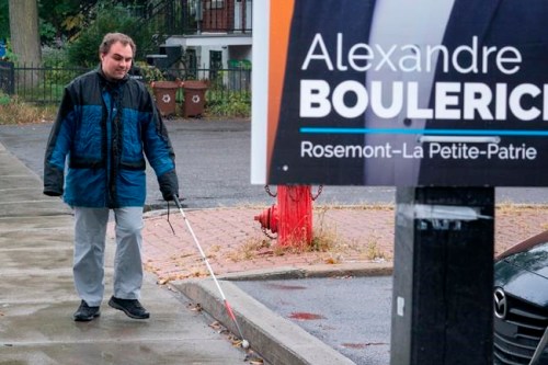 Jerome Plante, who is visually impaired, walks along a sidewalk towards a low-hanging election sign in Montreal on Tuesday, October 1, 2019. An advocacy group for the visually impaired is calling out political parties for their low-hanging Montreal election signs that create a hazard for those unable to see them. THE CANADIAN PRESS/Paul Chiasson