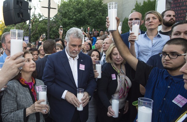 A demonstrator, right, raises a candle next to Quebec Premier Philippe Couillard moments before lunging on the Premier during a vigil for the victims of the shooting in Orando Thursday, June 16, 2016 in Montreal. THE CANADIAN PRESS/Paul Chiasson