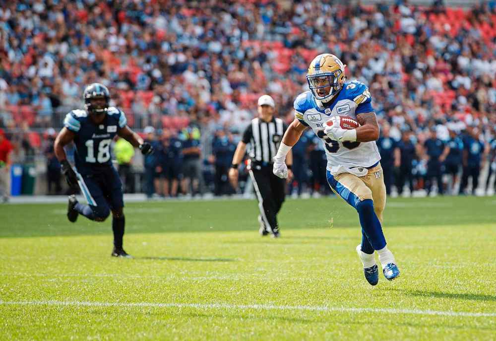 Toronto Argonauts Eric Striker, left, looks on as Winnipeg Blue Bombers' Andrew Harris scores a touchdown during first half CFL football action in Toronto on Saturday, July 21, 2018.