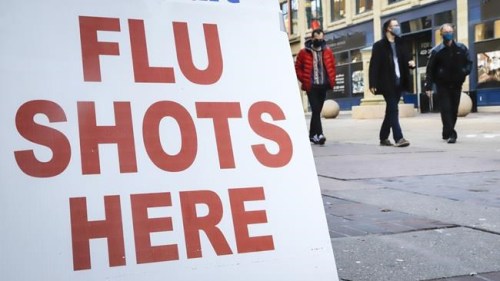 People wear masks as they pass a pharmacy offering flu shots in downtown Calgary, Alta., Friday, Oct. 30, 2020. Experts say a drastic drop in the circulation of the influenza virus this season means signs of flu are more likely to be COVID-19 than another respiratory virus.THE CANADIAN PRESS/Jeff McIntosh