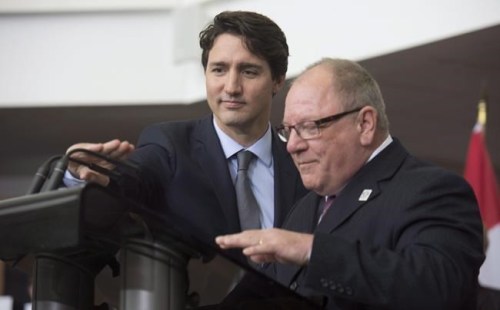 Prime Minister Justin Trudeau adjusts the microphones for Brian Bigger, Mayor of Sudbury, as he speaks during an event in Sudbury, Ont. Thursday April 7, 2016. Bigger is calling for stronger travel rules to control the spread of COVID-19 in northern Ontario. THE CANADIAN PRESS/Adrian Wyld