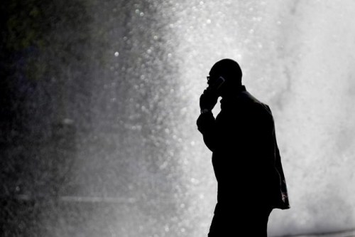 A pedestrian talking on a mobile phone is silhouetted in front of a fountain at John F. Kennedy Plaza in Philadelphia on October 11, 2012. THE CANADIAN PRESS/AP-Matt Rourke