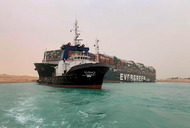 In this photo released by the Suez Canal Authority, a boat navigates in front of a cargo ship, Ever Given, Wednesday, March 24, 2021, after it become wedged across Egypt’s Suez Canal and blocked all traffic in the vital waterway. An Egyptian official warned Wednesday it could take at least two days to clear the ship. THE CANADIAN PRESS/Suez Canal Authority via AP