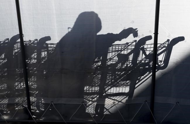 A worker casts a shadow as he sanitizes grocery carts in Toronto, Friday, Dec. 18, 2020. Despite being deemed essential and continuing to go into work as stay-at-home orders are renewed, most supermarket employees have yet to receive a vaccine or a pay boost. THE CANADIAN PRESS/Frank Gunn