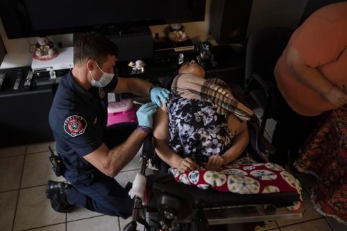 Torrance firefighter Trevor Borello, left, administers the second dose of the Pfizer COVID-19 vaccine to Barbara Franco, who suffers from muscular dystrophy, at her apartment, Wednesday, May 12, 2021, in Torrance, Calif. Teamed up with the Torrance Fire Department, Torrance Memorial Medical Center started inoculating people at home in March, identifying people through a city hotline, county health department, senior centers and doctor's offices, said Mei Tsai, the pharmacist who coordinates the program. (AP Photo/Jae C. Hong)