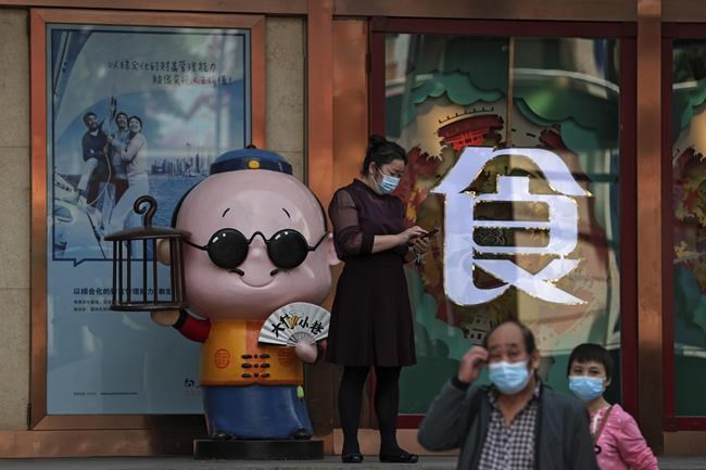 People wearing face masks to help curb the spread of the coronavirus walk by a worker browsing her smartphone outside a restaurant in Beijing, Monday, May 17, 2021. (AP Photo/Andy Wong)
