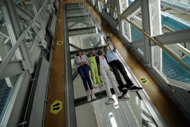 Visitors pose for photographs on the glass walkway at the Tower Bridge Visitor Attraction, in London, on the first day it was allowed to reopen as the British government relaxes its third coronavirus lockdown restrictions, Monday, May 17, 2021. (AP Photo/Matt Dunham)