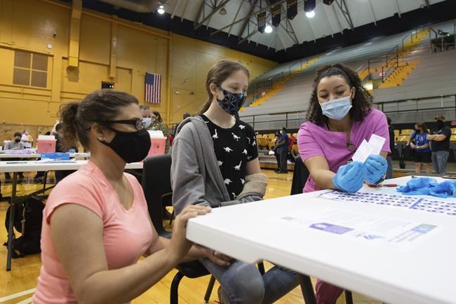 Eighth grader at Robinson Middle School, Jasic Helvey, 12, hears information about her COVID-19 vaccine Monday, May 17, 2021, at Topeka High School with by Shaunee Darrough, registered nurse with TrueCare Nursing, with her mom, Brandi Snyder, nearby. (Evert Nelson/The Topeka Capital-Journal via AP)