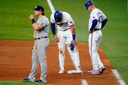New York Yankees first baseman Luke Voit, left, stands by as Texas Rangers first base coach Corey Ragsdale (43) checks on Joey Gallo, center, in the third inning of a baseball game in Arlington, Texas, Monday, May 17, 2021. Gallo, who earned a walk in the at-bat, stumbled on the bag looking back at the plate landing awkwardly on the ground. Gallo continued playing in the game. (AP Photo/Tony Gutierrez)