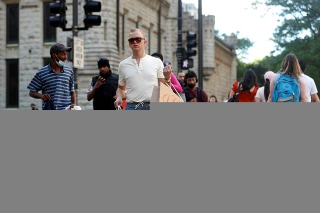 Troy Hemlin visiting Chicago from Springfield Il., crosses the street carrying shopping bags, Wednesday, May 26, 2021, in downtown Chicago. Americans are going back to one of their favorite past times: store shopping. With vaccinations rolling out and shoppers freer to go out maskless, retailers are seeing an eager return to their stores after months of watching their customers focus on online buying during the pandemic. (AP Photo/Shafkat Anowar)