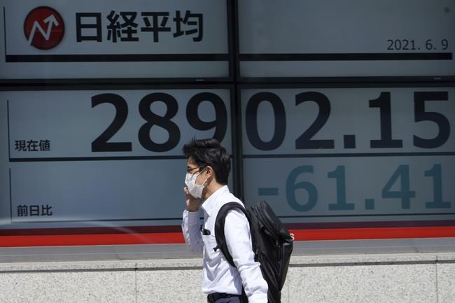 A man wearing a protective mask walks in front of an electronic stock board showing Japan's Nikkei 225 index at a securities firm Wednesday, June 9, 2021, in Tokyo. (AP Photo/Eugene Hoshiko)