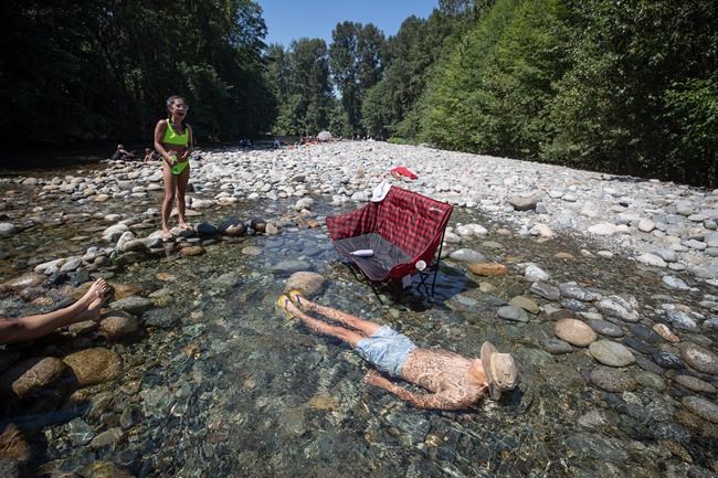 Albert Huynh cools off in the frigid Lynn Creek water as Leanne Opuyes, left, laughs in North Vancouver, B.C., on Monday, June 28, 2021. A stifling heat wave throughout much of Western Canada is unusual because of the nighttime temperatures it is bringing, says an expert. THE CANADIAN PRESS/Darryl Dyck