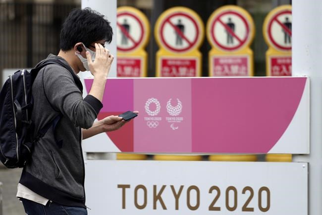 A man wearing a protective mask to help curb the spread of the coronavirus walks near an advertisement of Tokyo 2020 Olympic and Paralympic Games Tuesday, June 29, 2021, in Tokyo. (AP Photo/Eugene Hoshiko)