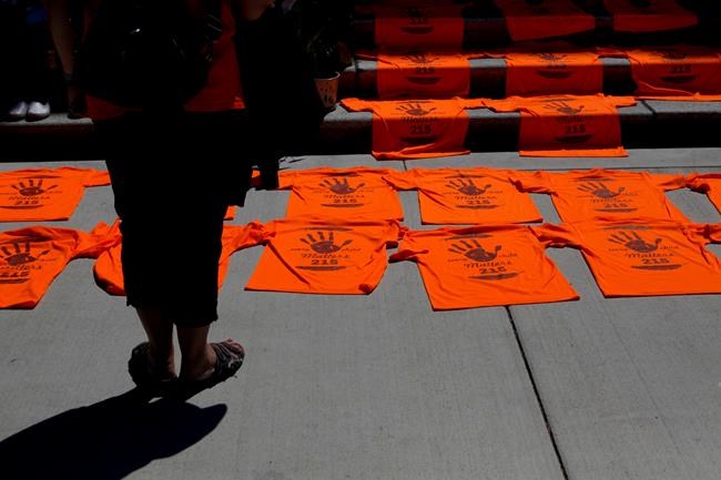 A woman looks over orange shirts, shoes, flowers and messages displayed on the steps outside the legislature in Victoria on Tuesday, June 8, 2021 following a ceremony in honour of the 215 residential school children whose remains were detected near a former residential school at Kamloops, B.C. The Lower Kootenay Band in B.C.'s southern Interior says a search using ground-penetrating radar has also found the remains of 182 people in unmarked graves at another residential school site.THE CANADIAN PRESS/Chad Hipolito