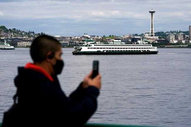 File-In this May 25, 2021 file photo a passenger wears a mask while riding on a Washington state ferry from Bremerton to Seattle as another ferry passes near the Space Needle, in Seattle. Washington and Oregon, which were among the first states to impose broad COVID-19 restrictions, on Wednesday, June 30, 201, lifted most rules to become among the last states to broadly ease pandemic orders put in place more than a year ago. (AP Photo/Ted S. Warren,File)