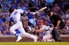 Chicago Cubs' Kris Bryant hits an RBI single off Philadelphia Phillies starting pitcher Aaron Nola as catcher J.T. Realmuto and home plate umpire Joe West watch during the third inning of a baseball game Tuesday, July 6, 2021, in Chicago. Rafael Ortega scored on the play. (AP Photo/Charles Rex Arbogast)