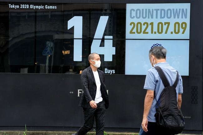 People wearing face masks walk past the countdown clock for the Tokyo 2020 Olympic Games near Shimbashi station Friday, July 9, 2021, in Tokyo. (AP Photo/Eugene Hoshiko)