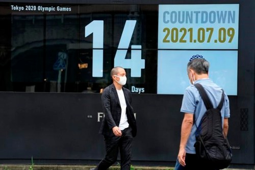 People wearing face masks walk past the countdown clock for the Tokyo 2020 Olympic Games near Shimbashi station Friday, July 9, 2021, in Tokyo. (AP Photo/Eugene Hoshiko)