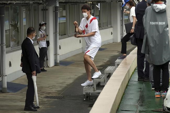 Former tennis player Shuzo Matsuoka, center, carries a lantern containing the Olympic Flame to Tokyo's fist leg of torch relay during the unveiling ceremony for Olympic Flame of the Tokyo 2020 Olympic torch relay at Komazawa Olympic Park, Friday, July 9, 2021, in Tokyo. Komazawa Olympic Park Stadium, where the flame unveiling ceremony took place, was used as one of the venues during the previous Tokyo Olympics held in 1964.(AP Photo/Eugene Hoshiko)