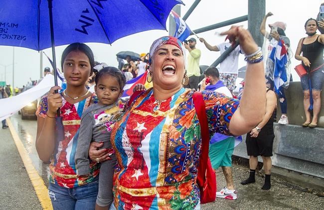 Monica Zerquera holds her daughter Khaily as her other daughter Melanie joins a group of Cuban exiles that blocked the Palmetto Expressway at Coral Way in support of protests in Cuba, Tuesday 13, 2021 in Miami. Demonstrators expressing solidarity with the thousands of Cubans who waged a rare weekend of protests around their island nation shut down a stretch of a major South Florida expressway Tuesday. (Pedro Portal/Miami Herald via AP)