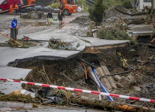 People carry their belongings past a broken road in Schuld, Germany, Friday, July 16, 2021. Two days before the Ahr river went over the banks after strong rain falls causing severals deaths and hundreds of people missing. (AP Photo/Michael Probst)