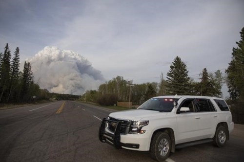 A Prince Albert police car is parked on Highway 55 as a plume of smoke rise from a forest fire burning northeast of the city in Prince Albert, Sask., Monday, May 17, 2021. The Saskatchewan Public Safety Agency has revoked a fire ban as cooler temperatures begin to prevail in the province. THE CANADIAN PRESS/Kayle Neis