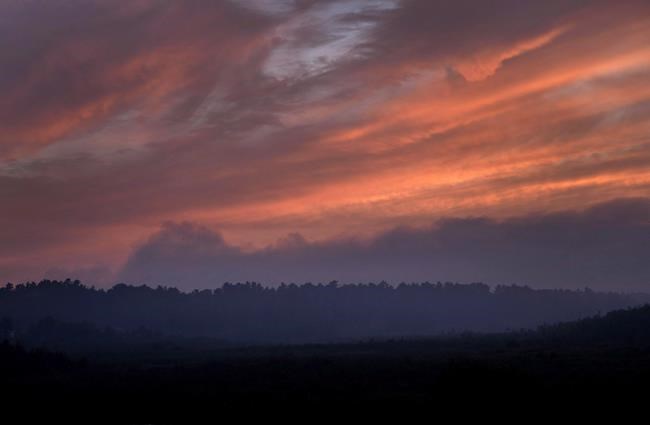Smoke hangs above the treeline near dusk blocking out the setting sun at forest fires near Killarney, Ont., Tuesday, July 31, 2018. THE CANADIAN PRESS/Fred Thornhill