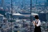 A person wearing a protective mask takes a picture from an observation deck as National Stadium, where the opening ceremony of the Tokyo 2020 Olympics will be held is seen in the background Saturday, July 10, 2021, in Tokyo. THE CANADIAN PRESS/AP, Kiichiro Sato