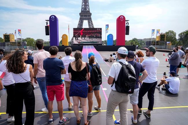 People watch on a giant screen the opening ceremony of the 2020 Summer Olympics in Tokyo, at the Trocadero gardens next to the Eiffel Tower in Paris, Friday, July 23, 2021. (AP Photo/Michel Euler)
