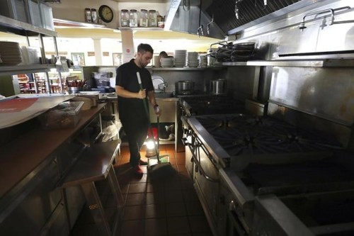 FILE - In this Oct. 10, 2019, file photo, Salvador Espinosa sweeps in the kitchen of a Mary's Pizza Shack restaurant during a Pacific Gas & Electric power shutdown in Santa Rosa, Calif. California utility regulators will hear from the state's largest electricity providers over steps taken to mitigate the use of planned power shutoffs, which regulators say should be used only as a last resort to prevent wildfires sparking from utility equipment. San Diego Gas & Electric briefs the Public Utilities Commission Monday, Aug. 2, 2021, with Southern California Edison and Pacific Gas & Electric up Tuesday. (Christopher Chung//The Press Democrat via AP, FIle)