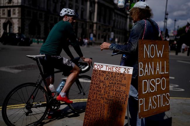 An environmental protester chats to a cyclist as he stands with placards and plastic bottles near the Houses of Parliament in London, Monday, Aug. 9, 2021. Earth's climate is getting so hot that temperatures in about a decade will probably blow past a level of warming that world leaders have sought to prevent, according to a report released Monday that the United Nations called a