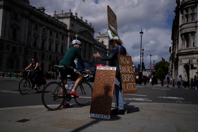 An environmental protester chats to a cyclist as he stands with placards and plastic bottles near the Houses of Parliament in London, Monday, Aug. 9, 2021. Earth's climate is getting so hot that temperatures in about a decade will probably blow past a level of warming that world leaders have sought to prevent, according to a report released Monday that the United Nations called a
