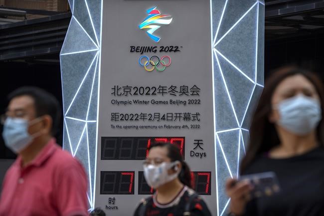 People wearing face masks to protect against COVID-19 walk past a display showing a countdown clock to the 2022 Winter Olympics in Beijing, Wednesday, Aug. 18, 2021. Beijing's top official is reiterating the need for strict anti-coronavirus measures at next year's Winter Olympics, now less than 200 days away, although it remains unclear whether spectators will be permitted. (AP Photo/Mark Schiefelbein)