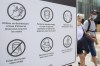 People wear face masks as they walk by a sign advising of COVID-19 prevention measures in Montreal on July 31, 2021. Canadians who refuse to wear a mask for non-medical reasons may be barred from casting ballots in person on Sept. 20. Chief electoral officer Stephane Perrault says in places where local public health rules require masking, Elections Canada will enforce those rules at polling locations. He encourages people who refuse to wear a mask to vote by mail instead. THE CANADIAN PRESS/Graham Hughes