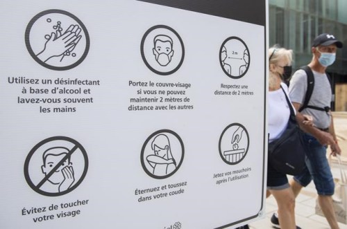People wear face masks as they walk by a sign advising of COVID-19 prevention measures in Montreal on July 31, 2021. Canadians who refuse to wear a mask for non-medical reasons may be barred from casting ballots in person on Sept. 20. Chief electoral officer Stephane Perrault says in places where local public health rules require masking, Elections Canada will enforce those rules at polling locations. He&nbsp;encourages people who refuse to wear a mask to vote by mail instead. THE CANADIAN PRESS/Graham Hughes