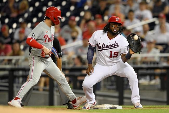 Philadelphia Phillies' Bryce Harper, left, is safe at first next to Washington Nationals first baseman Josh Bell (19) on a pick-off attempt during the third inning of a baseball game on Monday, Aug. 30, 2021, in Washington. (AP Photo/Nick Wass)