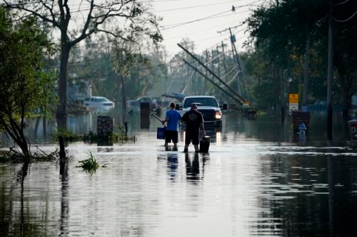 People walk up a street flooded in the aftermath of Hurricane Ida, Wednesday, Sept. 1, 2021, in Jean Lafitte, La. Louisiana residents still reeling from flooding and damage caused by Hurricane Ida are scrambling for food, gas, water and relief from the oppressive heat. (AP Photo/John Locher)