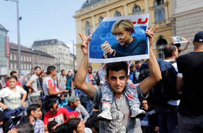 In this Sept. 4, 2015 file photo a migrant holds up a poster of German Chancellor Angela Merkel before starting a march out of Budapest, Hungary, towards Austria. In 2015, Merkel was the face of a welcoming approach to migrants as people fleeing conflicts in Syria and elsewhere trekked across the Balkans, allowing in hundreds of thousands and insisting that