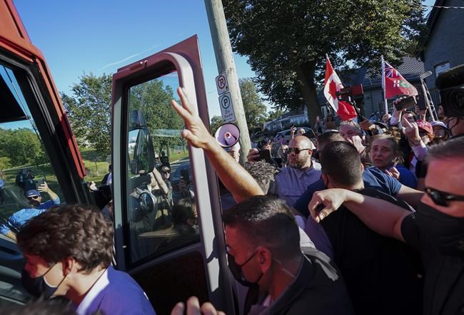 RCMP security detail put their hands up to protect Liberal Leader Justin Trudeau as protesters shout and throw gravel while leaving a campaign stop at a local microbrewery during the Canadian federal election campaign in London Ont., on Monday, September 6, 2021. THE CANADIAN PRESS/Nathan Denette